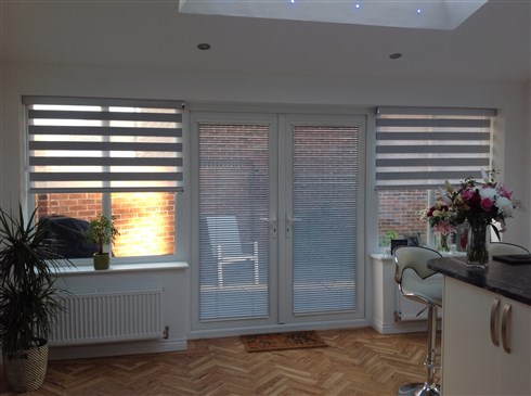 Grey Mirage roller blinds enhance this sunroom in Tyneside, matching Intu Venetians fit neatly into the glass space on the French doors giving full access to the garden without moving the blinds.